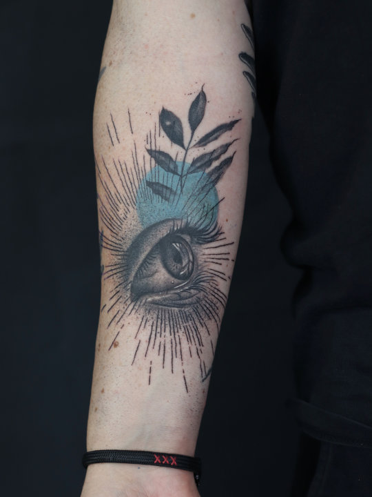tattoo of an eye in black and grey with leave and a colour circle